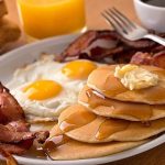 A delicous home style breakfast with crispy bacon, eggs, pancakes, toast, coffee, and orange juice.